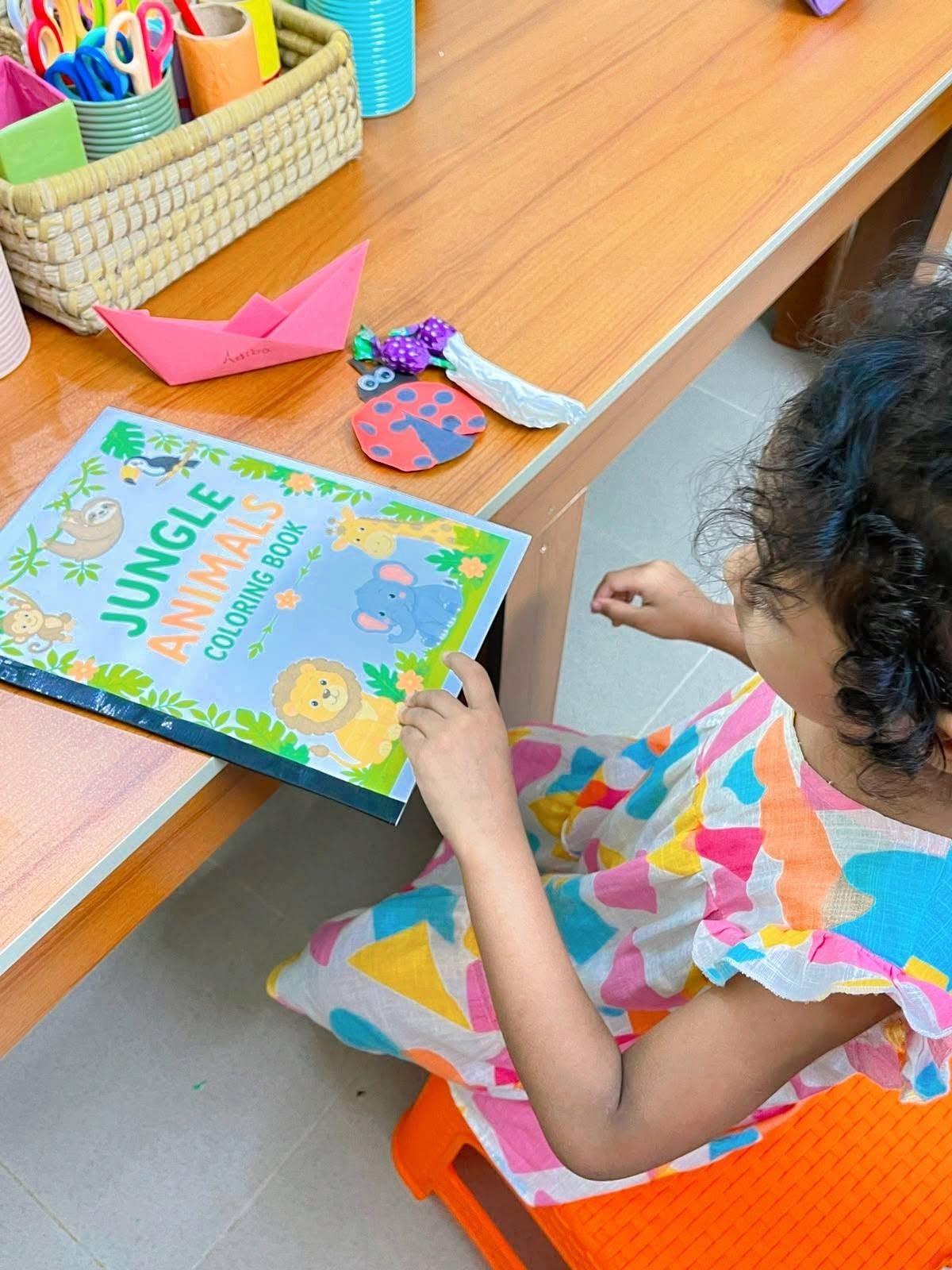 A child at a Creative Owls craft table with a coloring book and handmade paper crafts